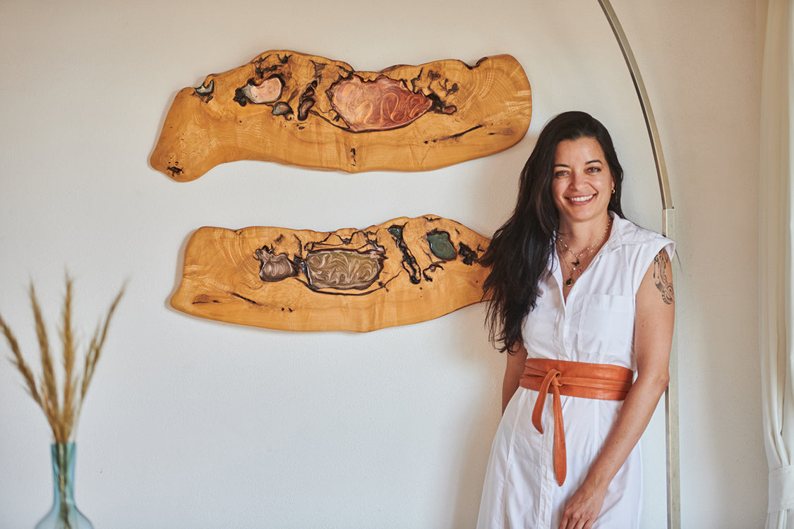 Woman standing indoors beside two handcrafted wooden wall art pieces featuring natural wood grain and resin inlays.