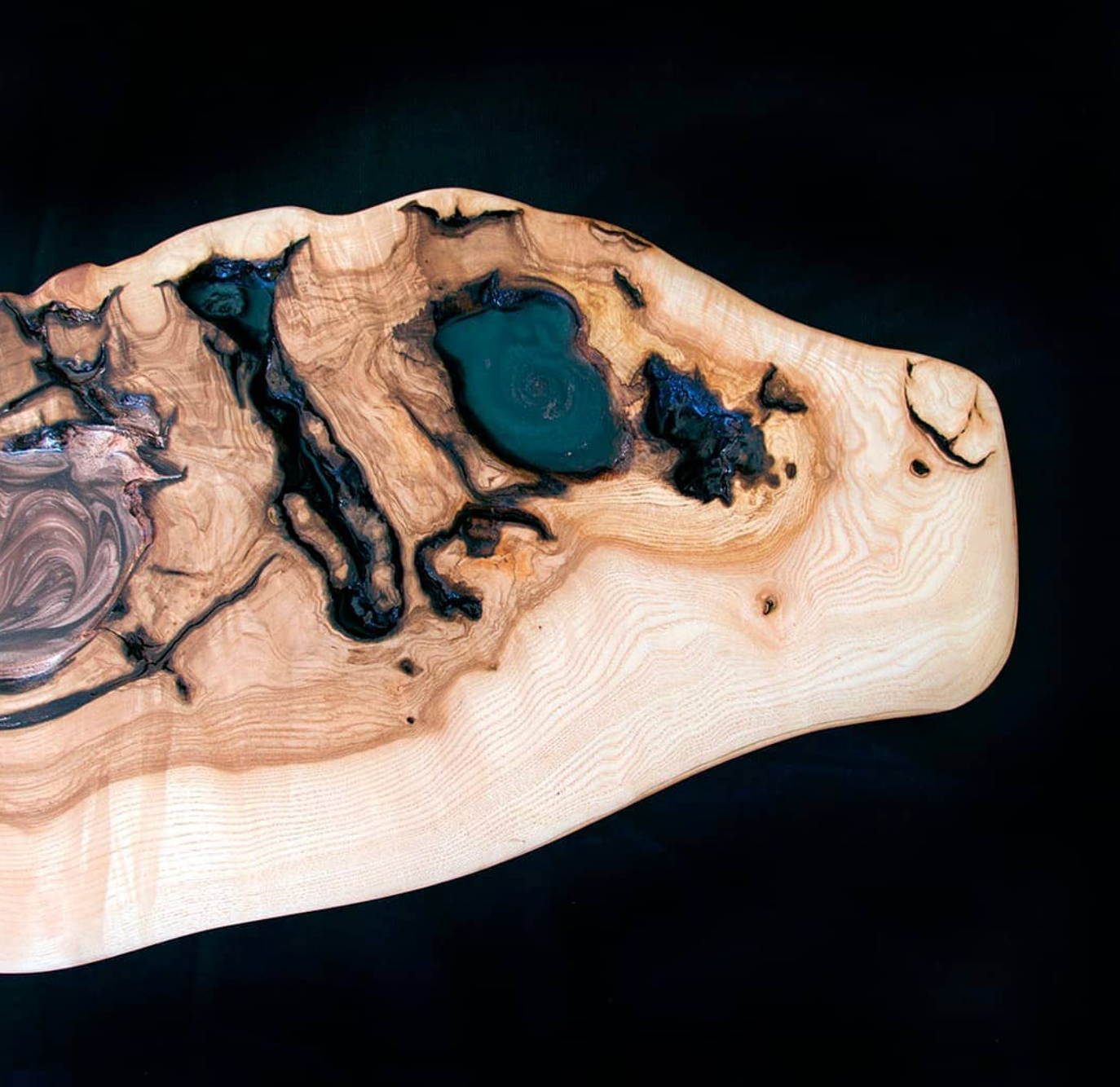 Irregularly shaped wooden slab with intricate grain patterns, enhanced by glossy green and metallic resin inlays, set against a black background.