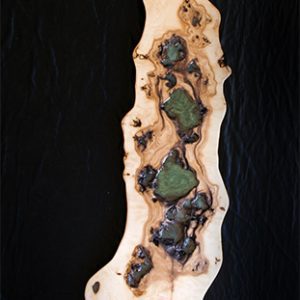 Escultura alargada y estrecha de madera y resina con múltiples cavidades y tonos verdes sobre fondo negro