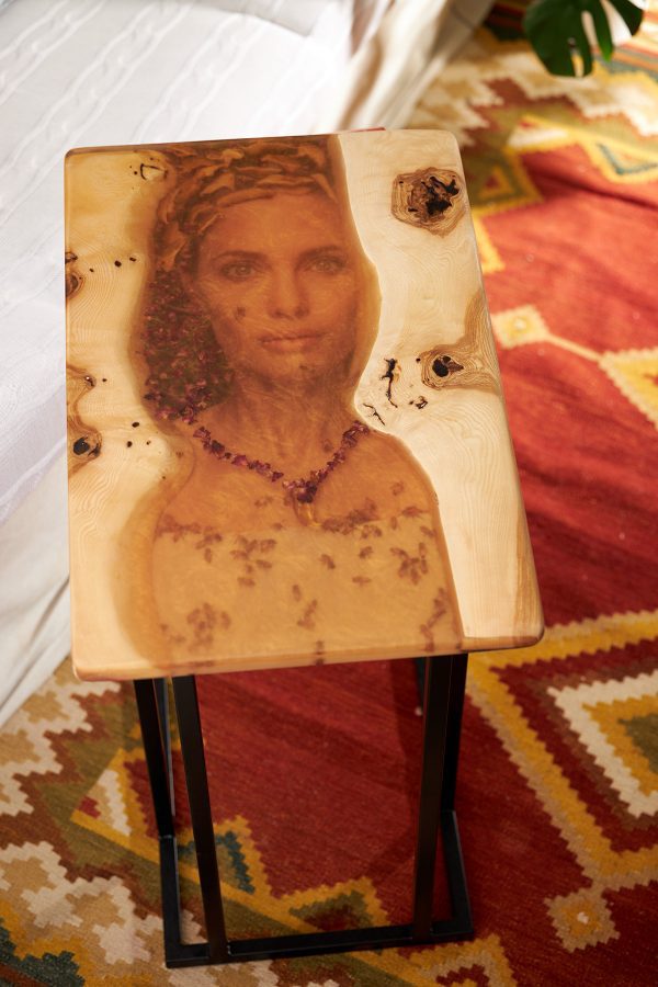 Mesa auxiliar con retrato de mujer impreso en resina, sobre un fondo de decoración interior."