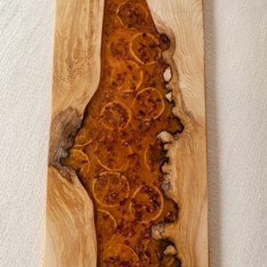Tabla de charcutería de madera artesanal con río de resina y rodajas de cítricos secos.