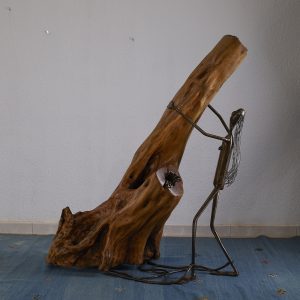 Escultura abstracta que combina madera natural y metal, representando una figura en actitud de liberación