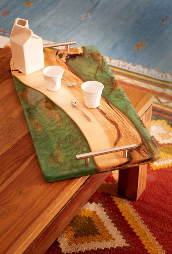 Tabla de servir de madera y resina verde con una jarra y tazas blancas, sobre una mesa de madera, interior hogareño.