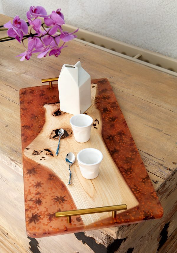 Mesa de servir con una jarra y tazas sobre una superficie de madera y resina, con flores de orquídea al fondo.