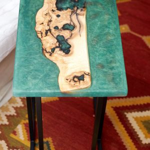 Mesa artística de madera y resina con incrustaciones turquesas sobre una base metálica moderna.