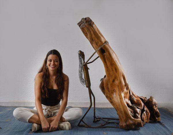 Artista sonriente sentada junto a una escultura de madera y metal