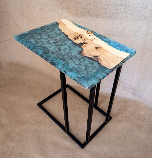 Mesa auxiliar de diseño exclusivo con superficie de resina azul y detalles de madera natural sobre patas de metal negro