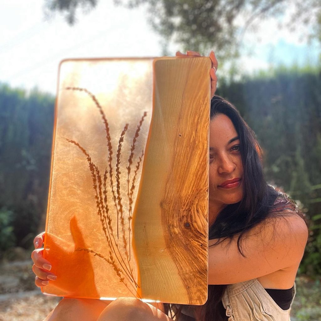 Mujer sosteniendo una pieza de arte de resina con inclusiones botánicas contra un fondo natural