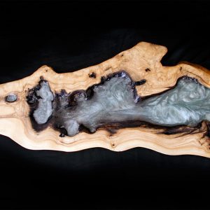 Repisa de madera con una secuencia de depósitos de resina gris y negra, evocando formaciones rocosas.
