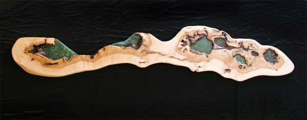 Elegante repisa de madera alargada con depresiones naturales llenas de resina verde que simulan un cañón visto desde arriba.