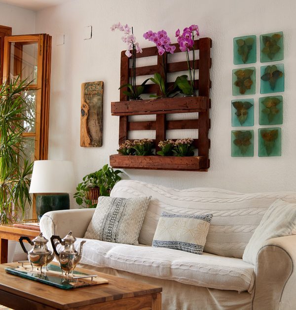 Ambiente luminoso y aireado de sala de estar con un cómodo sofá blanco, una variedad de plantas de interior y una colección de arte botánico cuadrado en la pared