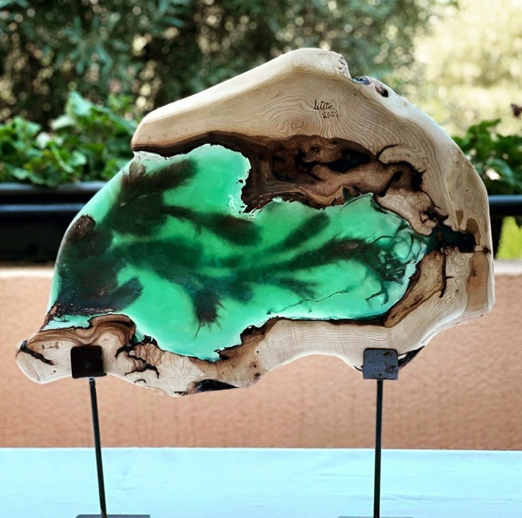 Escultura moderna de madera y resina verde sobre soporte metálico, mostrando la fusión de materiales.