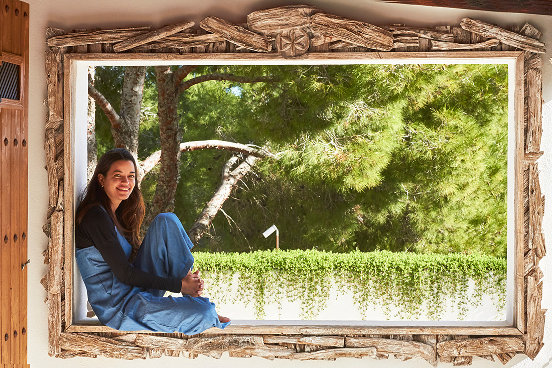 Mujer sonriente sentada en un alféizar de ventana de madera que da a un jardín verde