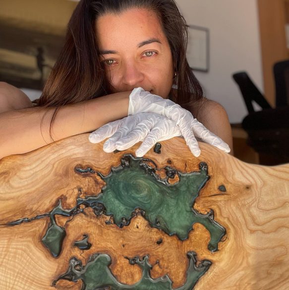 Mujer sonriente detrás de una obra de arte en madera y resina.
