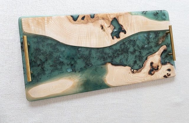 Bandeja de madera clara y resina verde azulado con aspecto de río, acentuada con asas metálicas doradas.