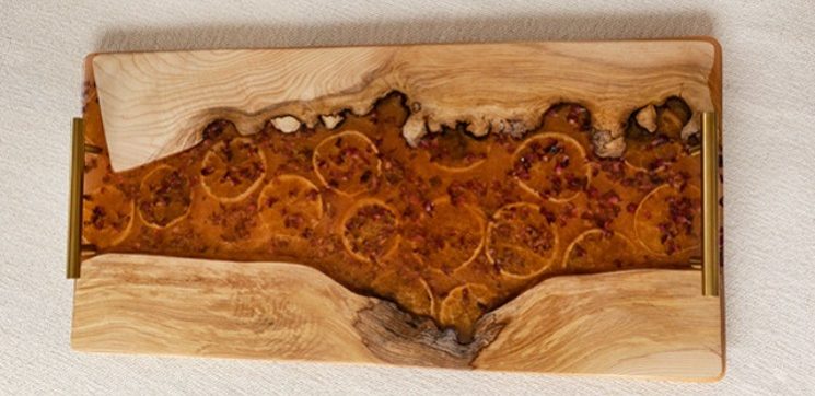 Bandeja de servir de madera natural con un río de resina ámbar que contiene rodajas de naranja incrustadas, realzada con asas metálicas doradas.