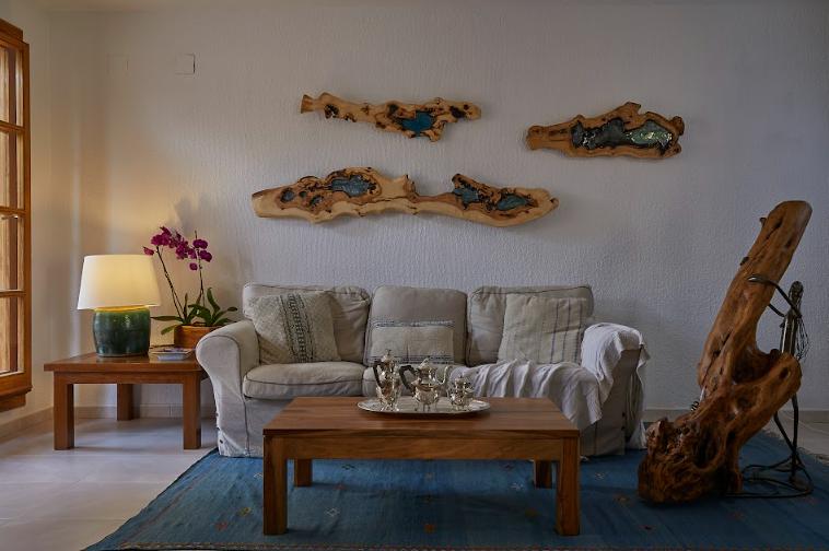 Sala de estar con muebles de madera, sofá beige, decoración de pared de madera con incrustaciones azules y lámpara de mesa verde sobre una alfombra azul.